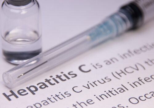 A close up of a dictionary definition of hepatitis C with a syringe and vial above it