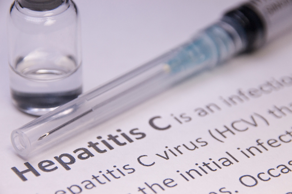 A close up of a dictionary definition of hepatitis C with a syringe and vial above it