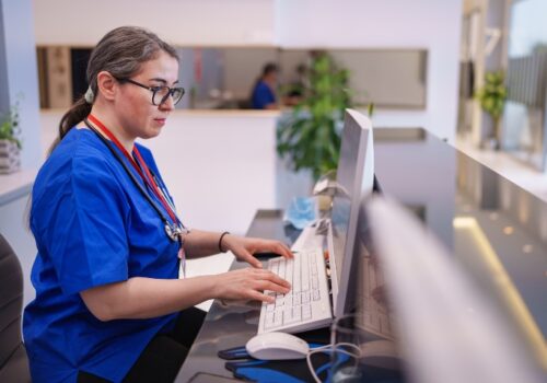 A clinician sitting at a desk in a hospital writing a letter to a patient on a computer