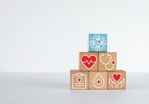 A blue block with an AI icon on top of a pyramid of wooden blocks containing medical symbols relating to heart health to illustrate machine learning-assisted mapping of VT ablation targets