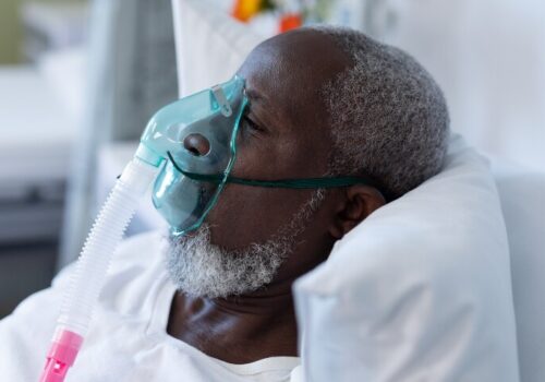 An old man laying in a hospital bed with an oxygen mask on to illustrate managing complex ventilatory failure beyond OSA