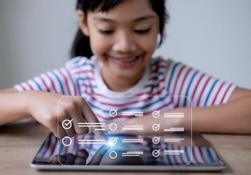 A young girl sitting at a desk with a tablet computer with a questionnaire tick box overlayed to illustrate a new P-POM for determining HRQOL in paediatric specialist care