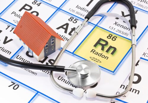 Model house and stethoscope placed on a periodic table background highlighting the element radon (Rn), symbolizing the lung cancer risks of residential radon exposure