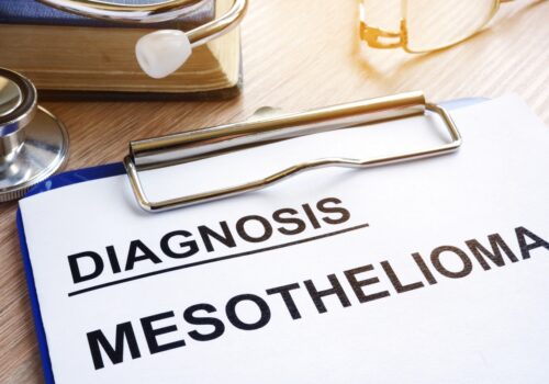 A piece of paper on a clipboard with the words diagnosis and mesothelioma surrounded by a book, stethoscope and glasses to illustrate a new trial investigating whether proton beam therapy can successfully be used to treat mesothelioma