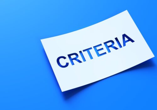 A white piece of paper with the word CRITERIA cut out of it on a blue background to illustrate that minimal disease activity criteria could support treat-to-target care for HS
